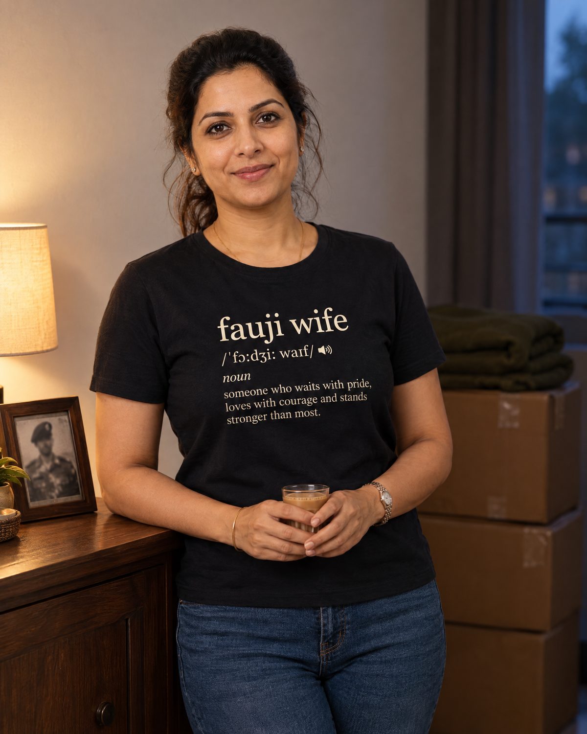 Woman holding a glass of chai at home beside posting boxes, wearing the Fauji Wife Dictionary tee